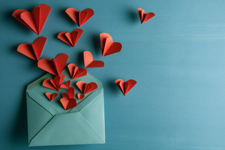 Red paper hearts flying out of an envelope on a blue wooden backgroundの素材