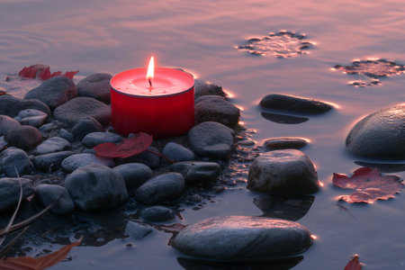 Red candle in water with pebbles and leaves in the foregroundの素材