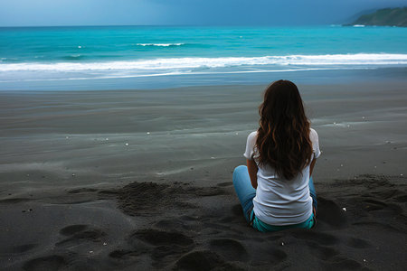 Young woman sitting on the beach and looking at the sea in the eveningの素材