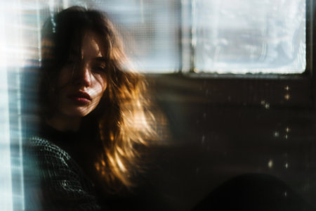 Portrait of a young woman looking through the window at home.の素材