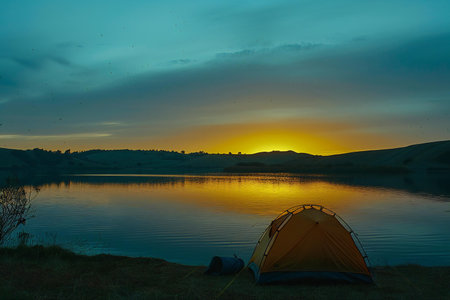 Camping on the shore of a lake at sunset. The tent is illuminated by the setting sun.の素材
