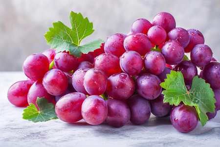 Ripe red grapes with green leaves on a white wooden background.の写真素材