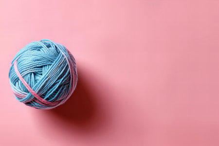 Ball of yarn on pink background, top view with copy space.