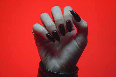 Female hand with black nail design. Glitter red nail polish manicure. Woman hand with black nail polish isolated on red background.の写真素材