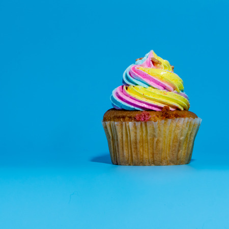 Colorful and enteresting cupcake isolated on blue background studio close up shot.