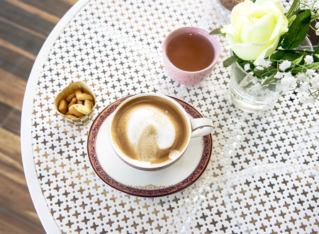 latte coffee cup on the white table serve with tea and small cracker. table decor by plastic flowerの写真素材