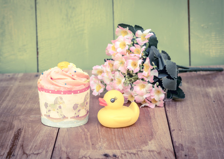 cup cake yellow duck and plastic flower on the wood boardの写真素材