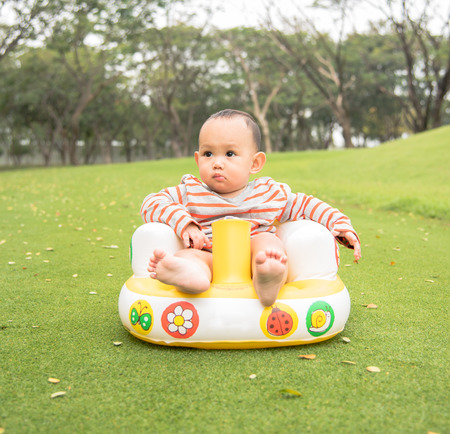 Outdoor portrait of Asian baby boy playing sitting and crawling on the green grass field in the parkの写真素材