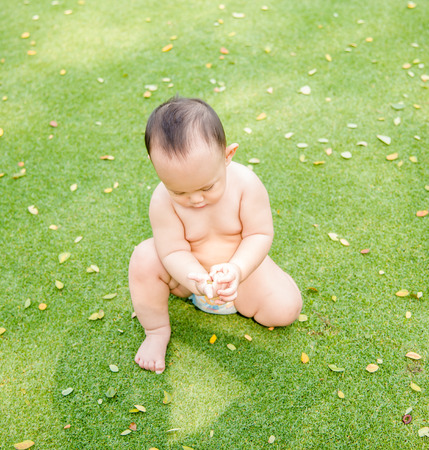 Outdoor portrait of Asian baby boy playing sitting and crawling on the green grass field in the parkの写真素材