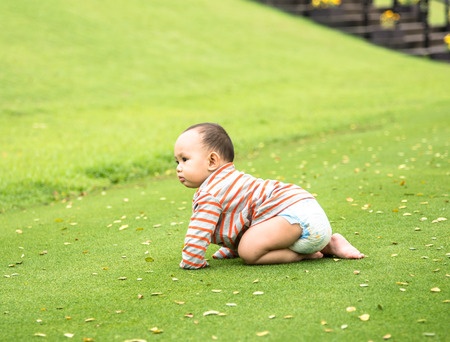 Outdoor portrait of Asian baby boy playing sitting and crawling on the green grass field in the parkの写真素材