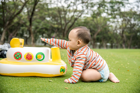Outdoor portrait of Asian baby boy playing sitting and crawling on the green grass field in the parkの写真素材