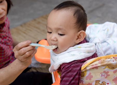 Baby eating food by mother feeding, family scene of Thailandの写真素材