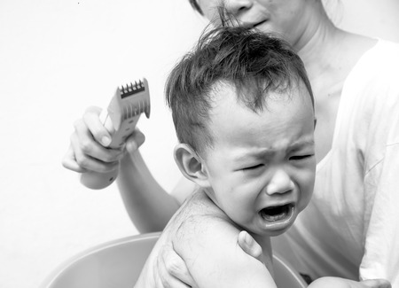 black and white photography of Thai baby feel scare of hair clipper when  mother cutting his hairの写真素材
