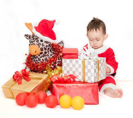 Kid in the red Santa Claus suit sitting with reindeer doll among the gift boxesの写真素材