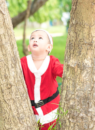 Asian baby boy in santa claus suit is playing with reindeer doll at outdoor parkの写真素材