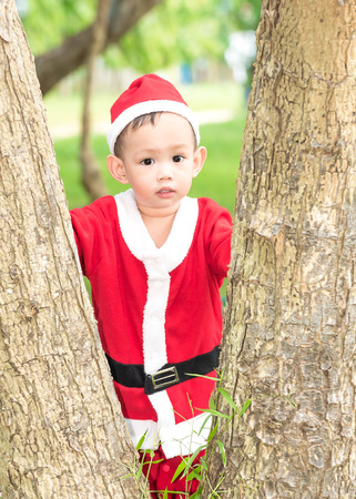 Asian baby boy in santa claus suit is playing with reindeer doll at outdoor parkの写真素材