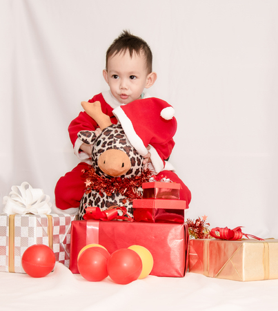 Kid in the red Santa Claus suit sitting with reindeer doll among the gift boxesの写真素材