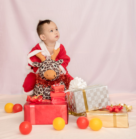 Kid in the red Santa Claus suit sitting with reindeer doll among the gift boxesの写真素材
