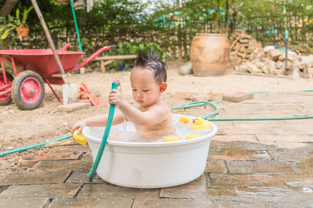 Asian baby boy outdoor bathing in the white bathtub . He is smiling and playing yellow duck full of happiness, Country side culture of Thailandの写真素材