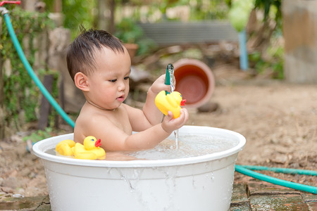 Asian baby boy outdoor bathing in the white bathtub . He is smiling and playing yellow duck full of happiness, Country side culture of Thailandの写真素材