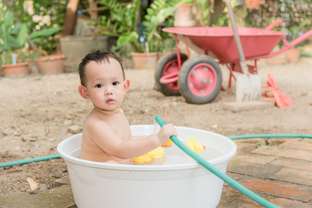 Asian baby boy outdoor bathing in the white bathtub . He is smiling and playing yellow duck full of happiness, Country side culture of Thailandの写真素材