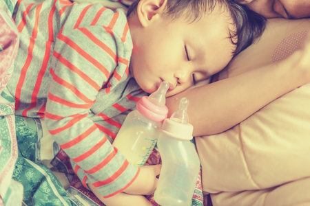 Baby milk bottle and water bottle holdind by asian baby boy. Asian baby boy sleeping in mother armの写真素材