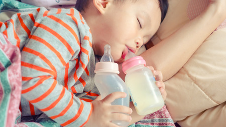 Baby milk bottle and water bottle holdind by asian baby boy. Asian baby boy sleeping in mother armの写真素材