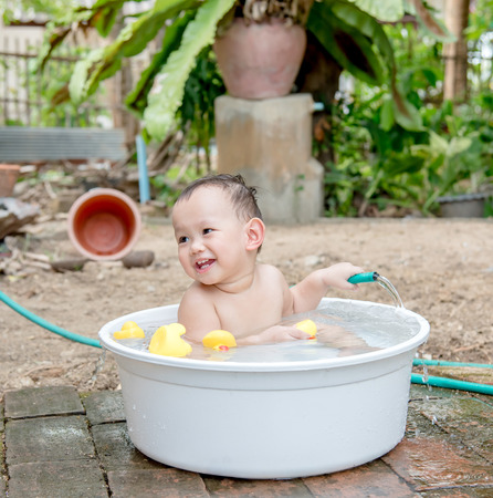 Asian baby boy outdoor bathing in the white bathtub . He is smiling and playing yellow duck full of happiness, Country side culture of Thailandの写真素材