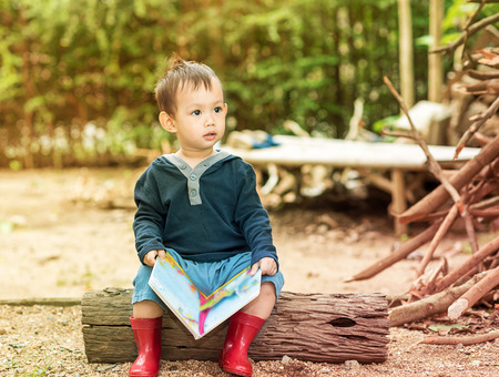 Asian baby boy  reading tale book , Boy wear red boot sitting on a log .の写真素材