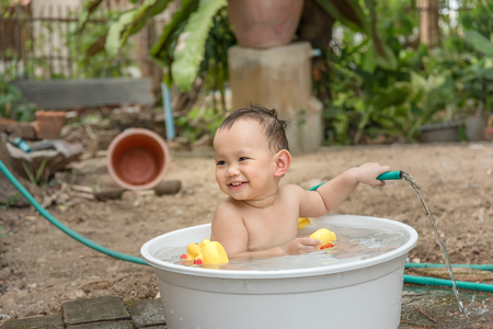 Asian baby boy outdoor bathing in the white bathtub . He is smiling and playing yellow duck full of happiness, Country side culture of Thailandの写真素材