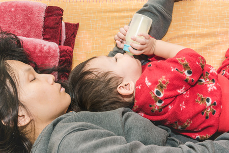 Asian mother holding baby in arm while  baby drinking milk from bottle while sleeping