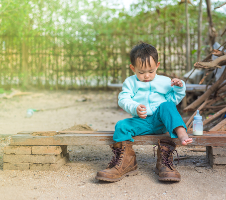 Thai Baby boy try to  wearing father's boots while drinking milk from bottle.の写真素材