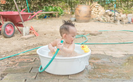 Asian baby boy outdoor bathing in the white bathtub . He is smiling and playing yellow duck full of happiness, Country side culture of Thailandの写真素材