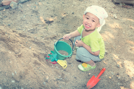 Thai baby boy palying on  pile of sand with toy and plastic fork, spoonの写真素材