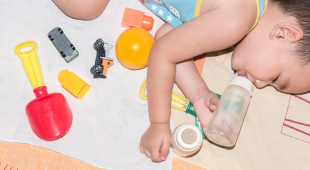Asian baby boy laying on bed with his toy while drinking water from milk bottleの写真素材