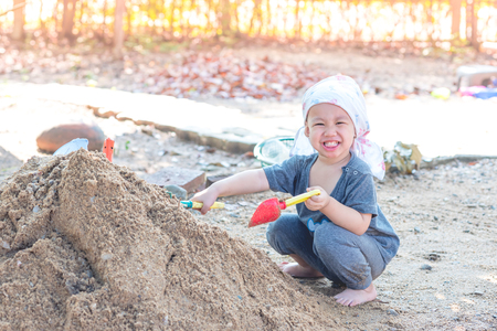 Thai baby boy palying on  pile of sand with toy and plastic fork, spoonの写真素材