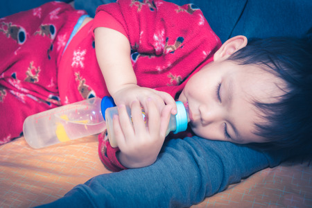 Asian baby drinking milk from bottle while sleepingの写真素材