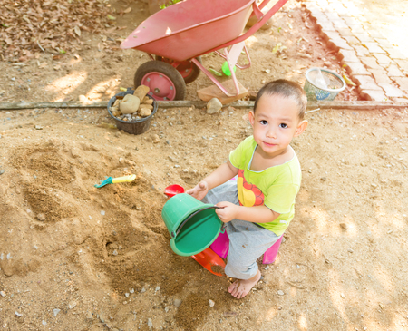Thai baby boy palying on  pile of sand with toy and plastic fork, spoon , truck ,wheel barrowの写真素材