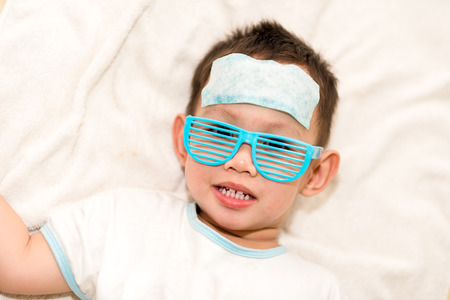 Asian boy having fever . The kid attach cooling gel pad on his forehead for relief feverの写真素材