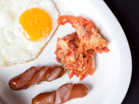 fried egg sausage and Kimchi  serve as  breakfast  in white dishの写真素材