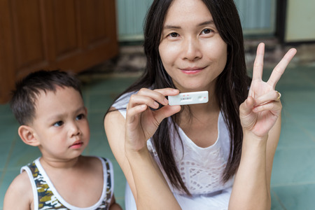 Young Asian mother holding pregnant tester on her hand, feeling happy for new coming baby