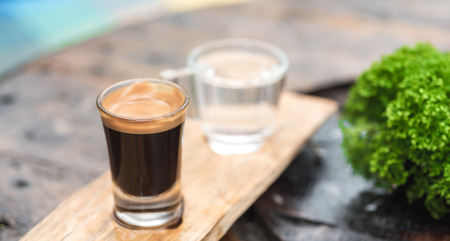 Espresso coffee cup serve with glass of water on wooden table which decor by green plantの写真素材