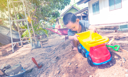 Thai baby boy palying on  pile of sand with toy and plastic fork, spoon , truck ,wheel barrowの写真素材