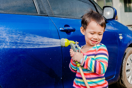 Asian baby boy washing blue car by green water sprayerの写真素材