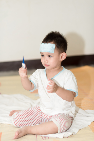 Asian boy having fever . The kid attach cooling gel pad on his forehead for relief feverの写真素材