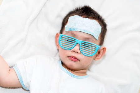 Asian boy having fever . The kid attach cooling gel pad on his forehead for relief feverの写真素材