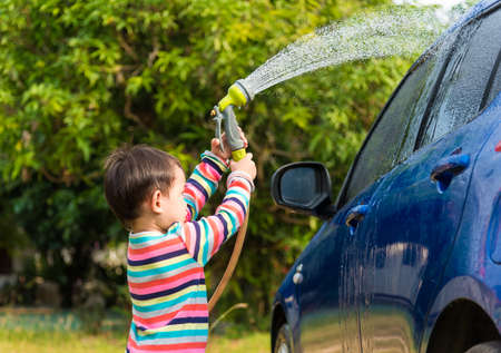 Asian baby boy washing blue car by green water sprayerの写真素材