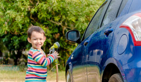 Asian baby boy washing blue car by green water sprayerの写真素材