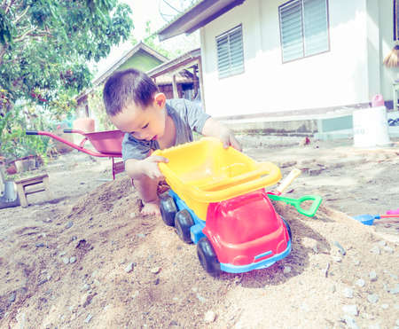 Thai baby boy palying on  pile of sand with toy and plastic fork, spoon , truck ,wheel barrowの写真素材