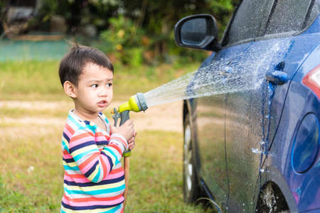 Asian baby boy washing blue car by green water sprayerの写真素材